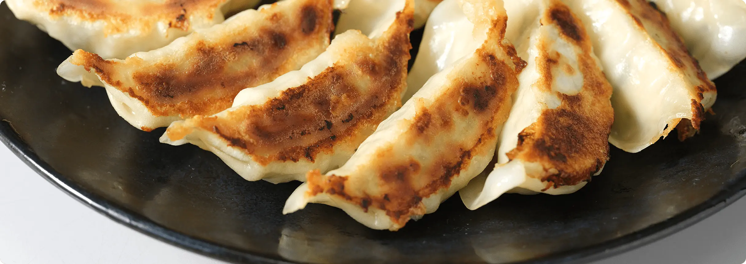 黒い皿に盛られた焼き目のきれいな餃子の写真